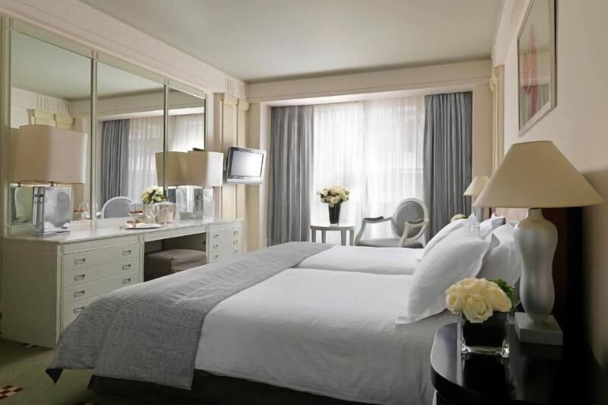 A hotel room with a bed, a desk with a mirror, a television, and a chair.