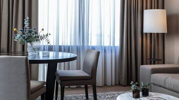 A hotel room with a dining table, two chairs, a sofa, a coffee table, and a lamp.