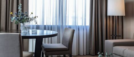 Una habitación de hotel con una mesa de comedor, dos sillas, un sofá, una mesita de centro y una lámpara.