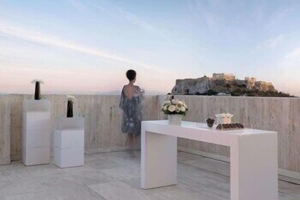 A terrace with a white table, two white pedestals, and a person in a dress.