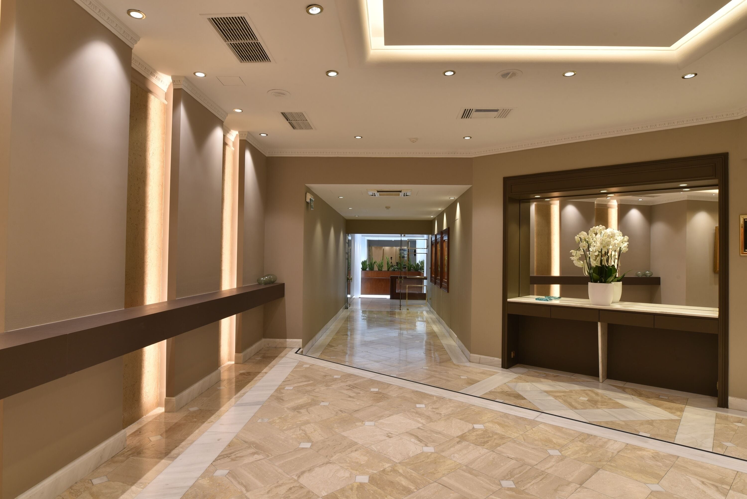 A hotel corridor with a marble floor, a long reception desk, and a large mirror.