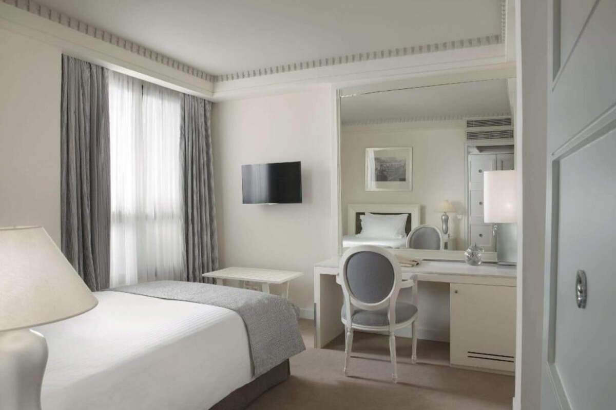 A hotel room with a bed, a desk, a chair, a television, and a door.