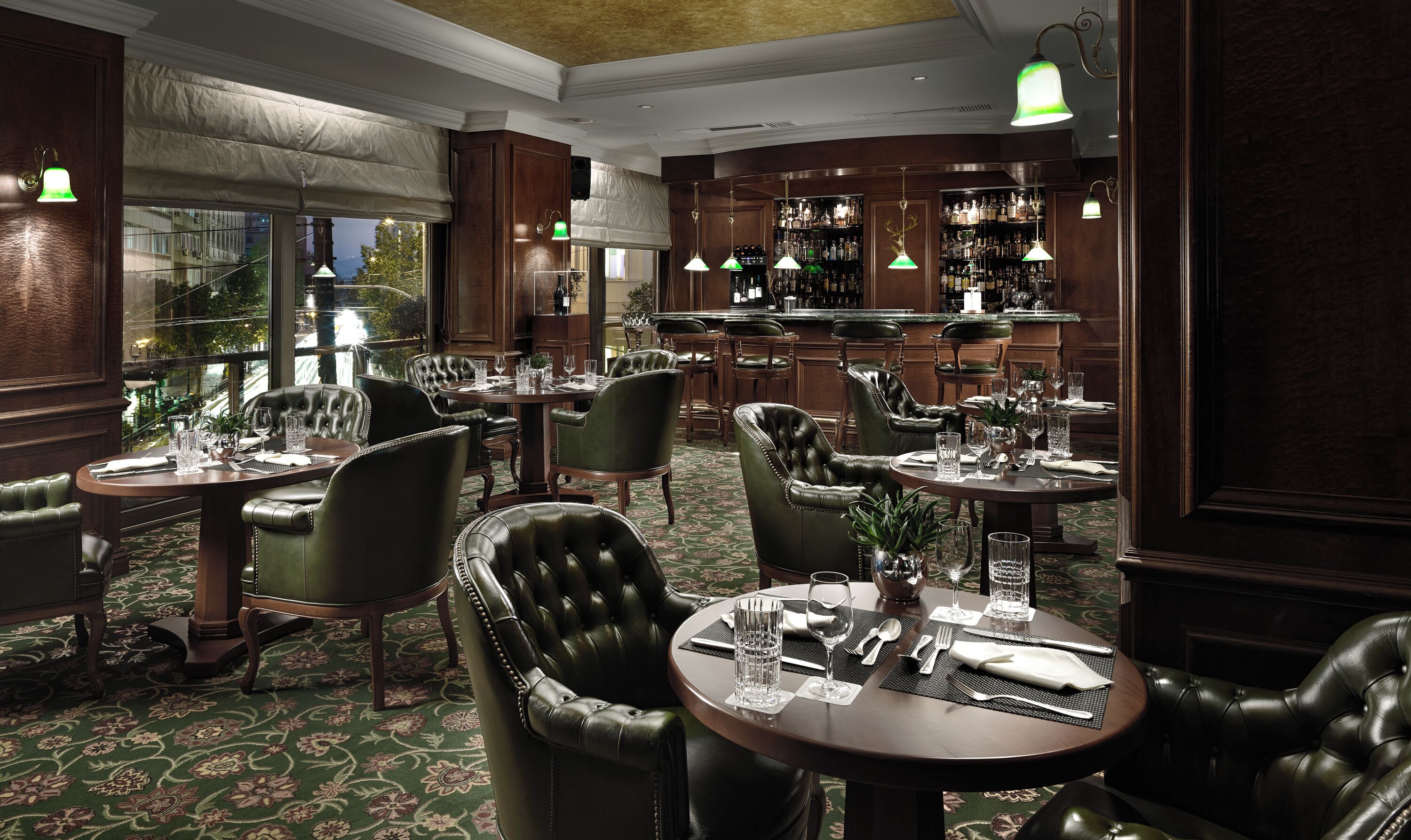 Ein formeller Speisesaal mit Ledersesseln und Tischen, eine Bar mit Flaschenregalen und Blick durch große Fenster.