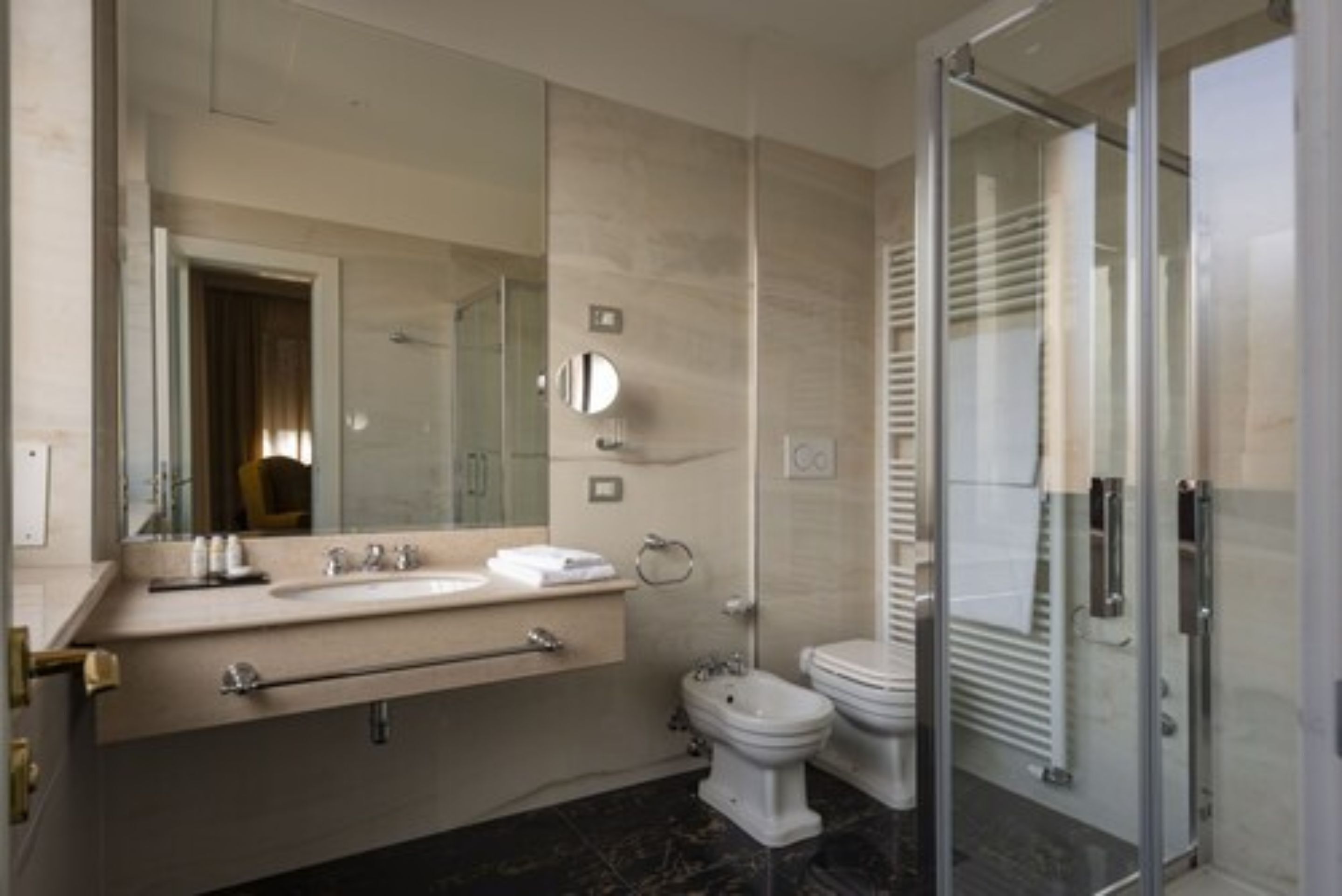 A modern bathroom with a glass shower enclosure, a large mirror, and a vanity with a sink and towel rack.