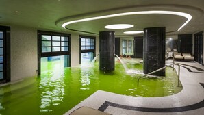 Ein Hallenbad mit klarem Wasser, großen Fenstern und modernen Beleuchtungselementen.