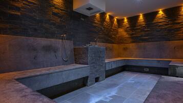 Un spa moderno con paredes de piedra y bancos, una bañera hidromasaje integrada y zona de ducha.