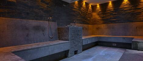 A modern spa with stone walls and benches, a built-in hot tub, and a shower area.