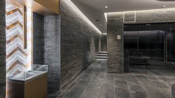 A modern hallway with dark stone walls, a herringbone patterned wall, and a glass enclosure with a metal frame.