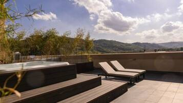 Una terrazza sul tetto con vasca idromassaggio, poltrone relax e vista su un paesaggio montuoso.