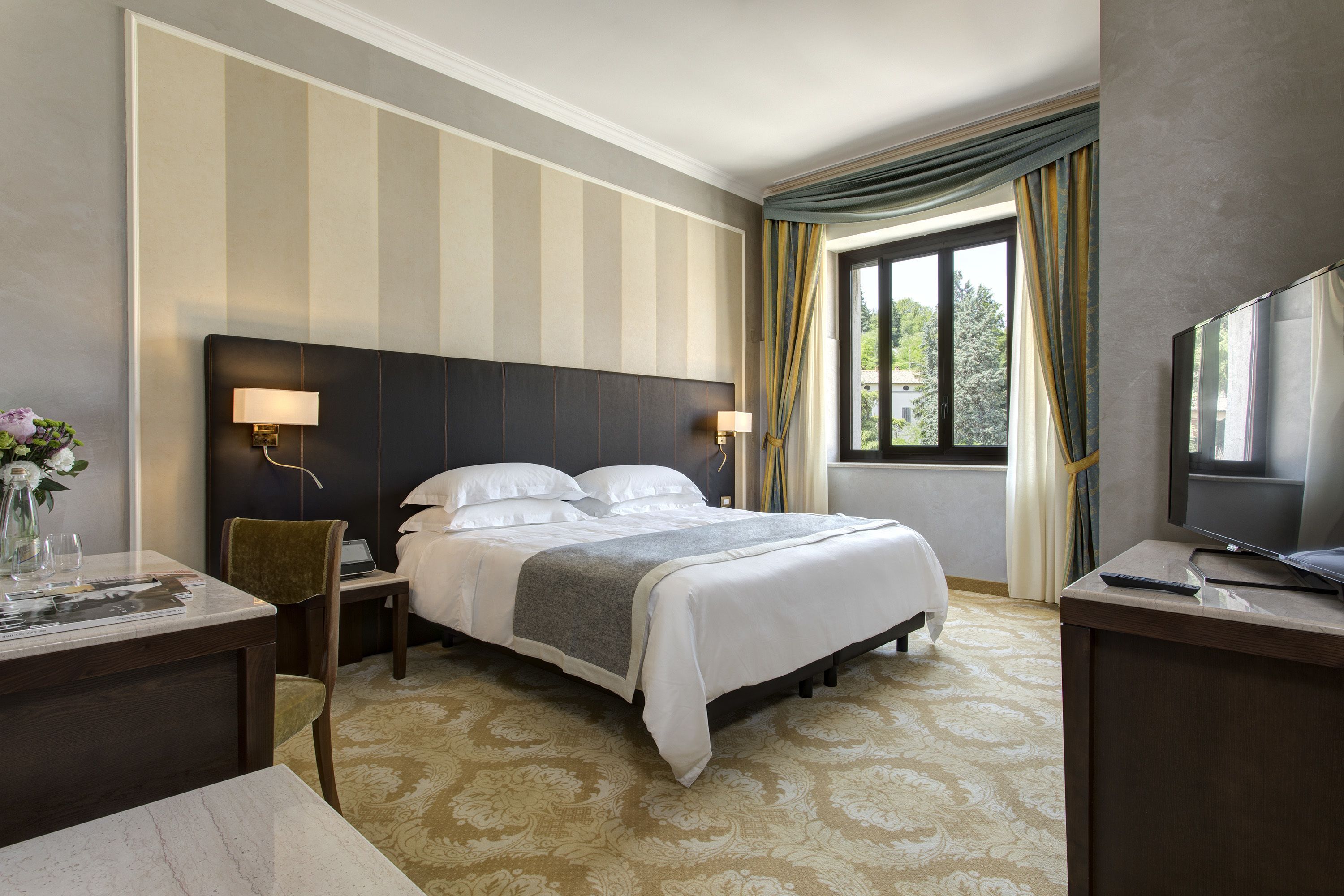 A hotel room with a large bed, a desk with a chair, a television, and a window with curtains.