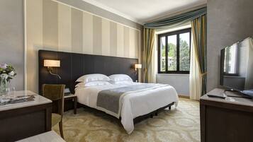A hotel room with a large bed, a desk with a chair, a television, and a window with curtains.