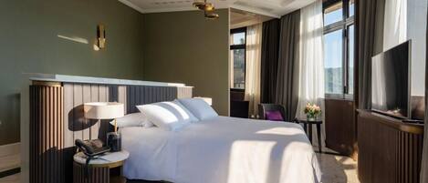 A hotel room with a large bed, a bedside table with a lamp, a TV, and a view of the outdoors.