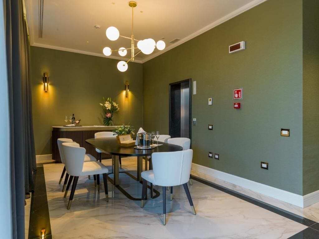 Un comedor con una mesa redonda, sillas blancas, una araña y un detector de incendios instalado en la pared.