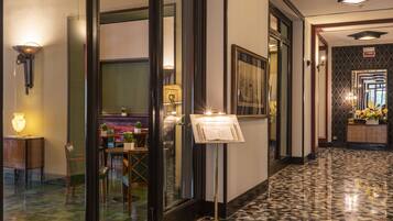 A hotel corridor with a patterned floor, a reception desk, a dining area, and a mirror with a decorative frame.