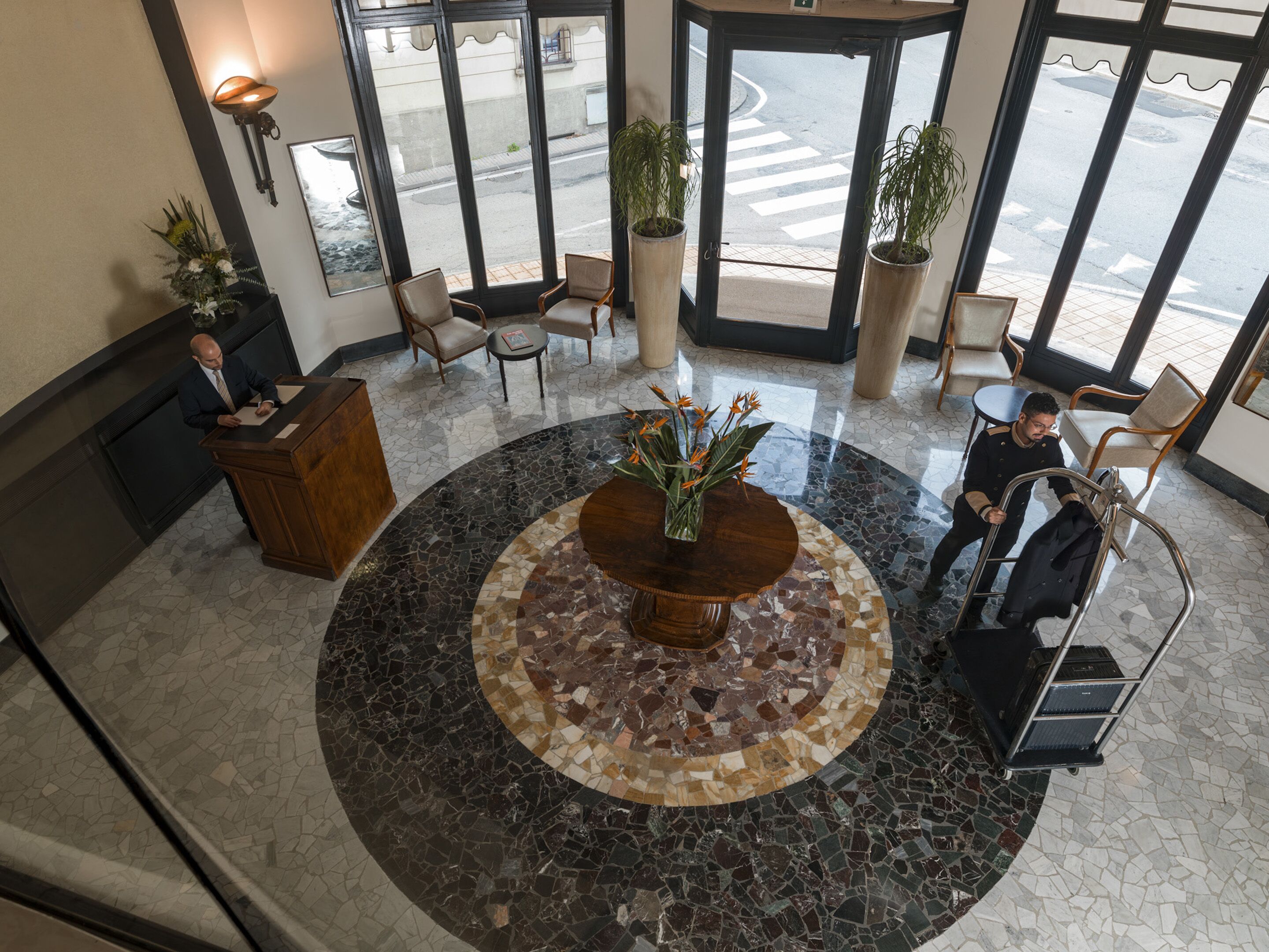 A lobby with a central mosaic table, seating area, and large windows.
