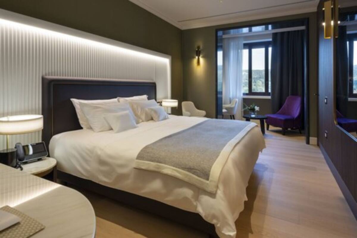 Ein modernes Hotelzimmer mit einem großen Bett, Nachttischen, einem Schreibtisch und einer Sitzecke mit Sesseln.