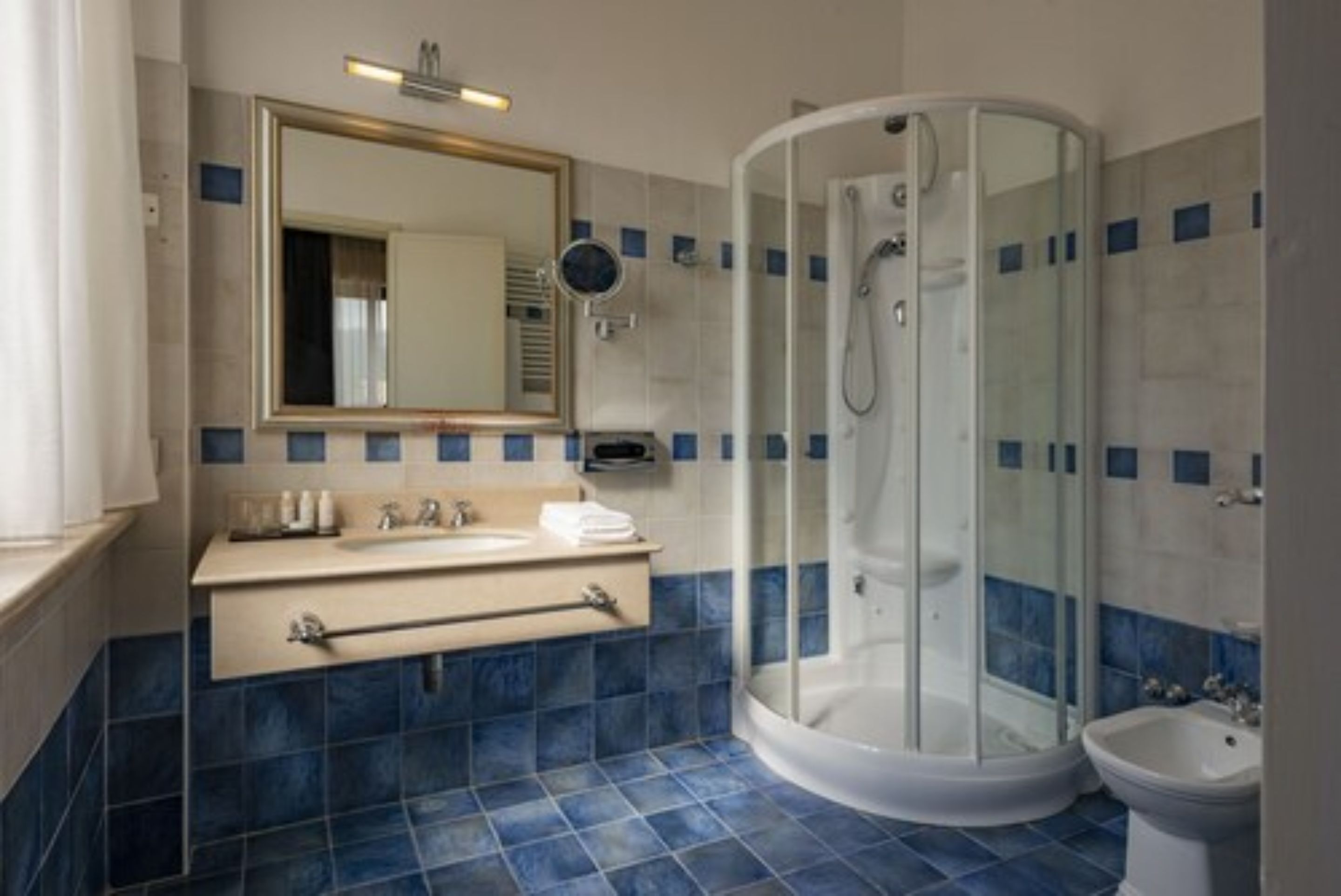 A modern bathroom with a curved glass shower enclosure, a sink with a towel rack, and a mirror above the sink.