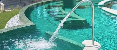 A swimming pool with a clear blue water feature, a metal ladder, and a white deck surrounding it.
