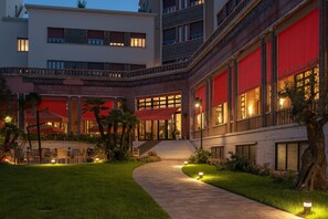 Une cour d’hôtel avec un chemin pavé, un espace extérieur aménagé avec des sièges et un escalier menant à l’entrée.