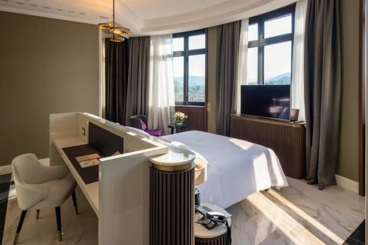 Ein Hotelzimmer mit Bett, Schreibtisch, Stuhl, Fernseher und Blick ins Freie.