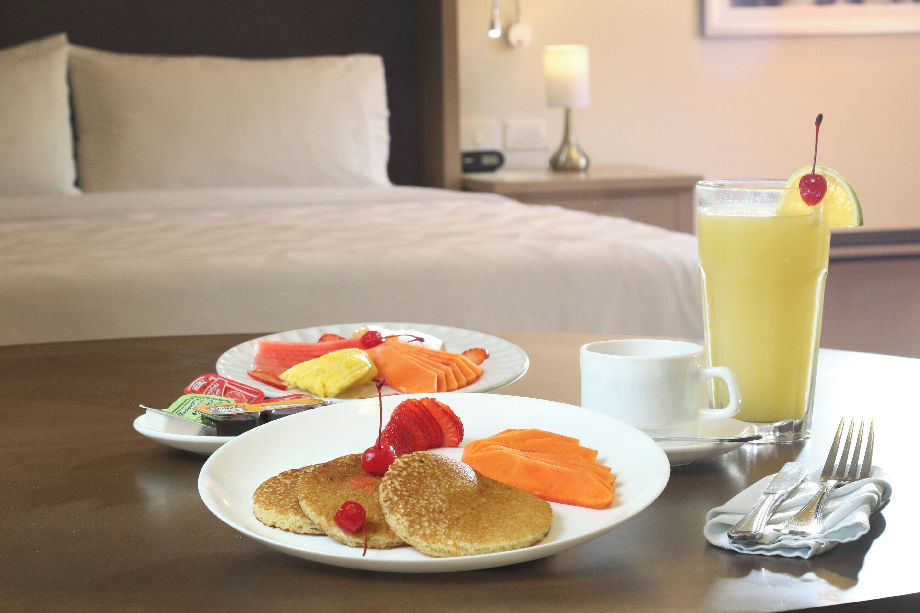 A breakfast setting with pancakes, fruit, and a glass of orange juice on a table.