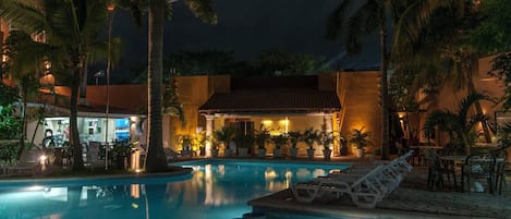 A nighttime pool area with lounge chairs, palm trees, and a building with warm lighting.