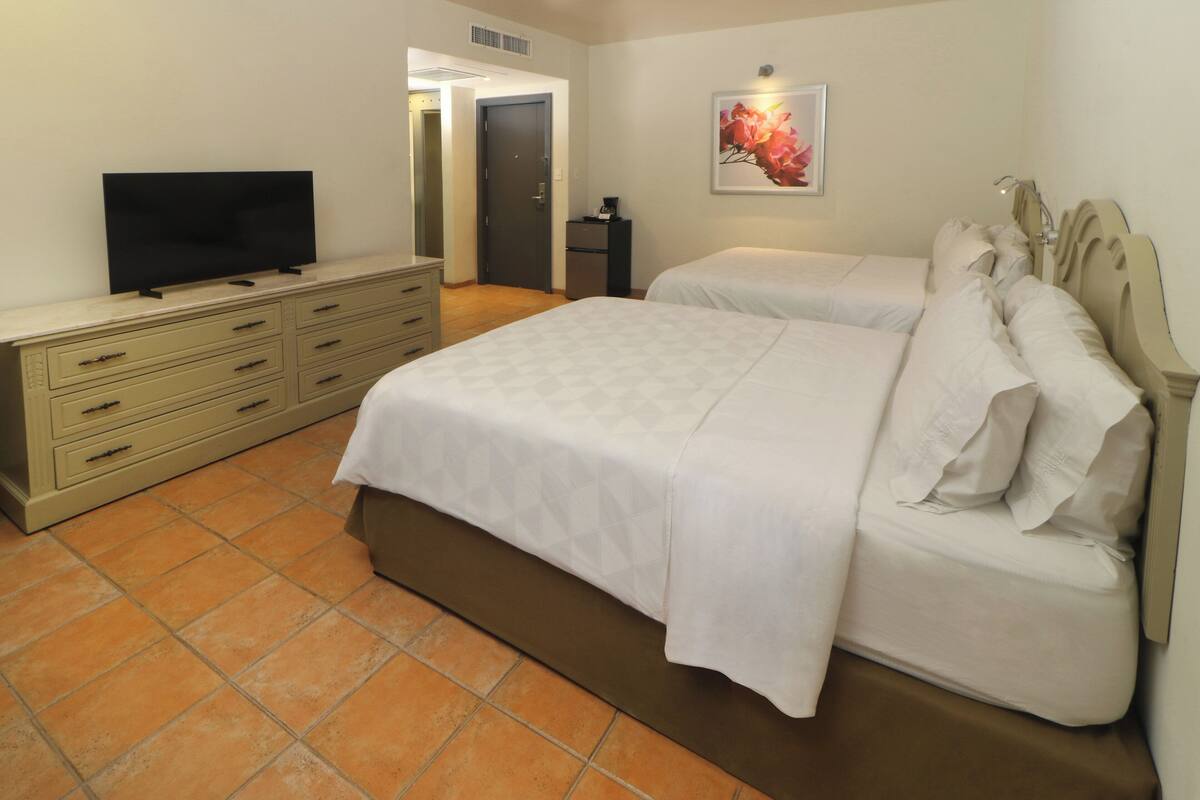 Habitación de hotel con una cama grande, un televisor en una cómoda y una puerta que da a otra habitación.