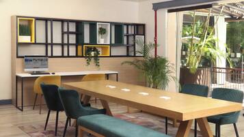 A modern meeting room with a long wooden table, green upholstered chairs, and a built-in bookshelf with plants.