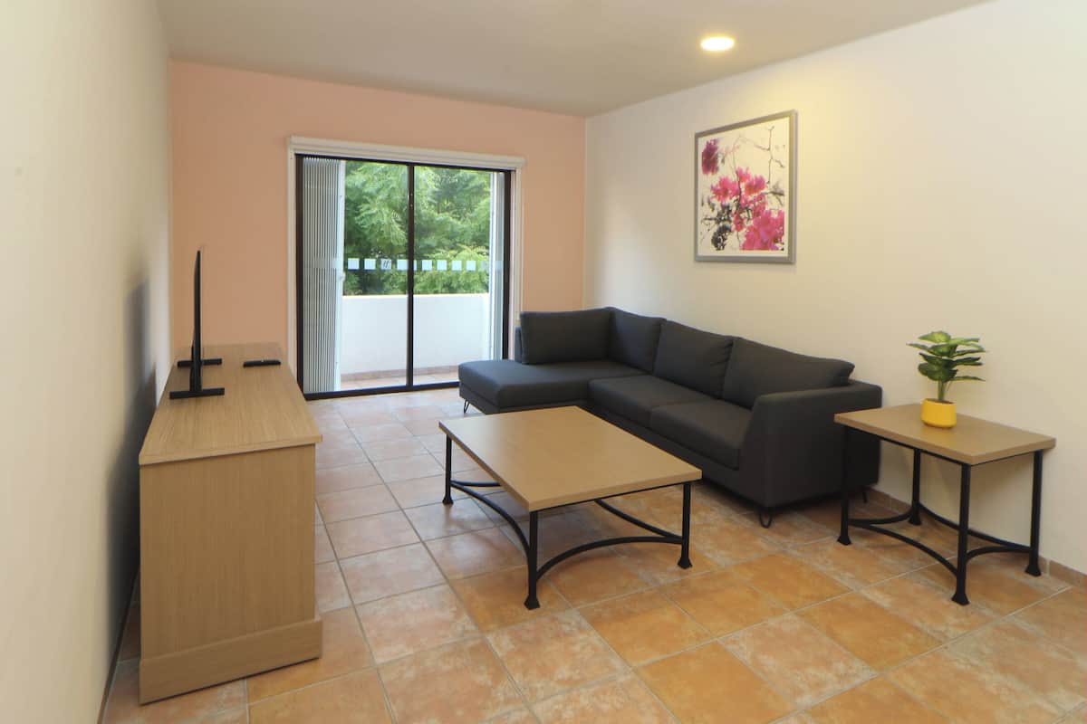 Una sala moderna con un sofá, una mesa de centro, una pequeña mesa con una planta y un ventanal corredero que da a un balcón.