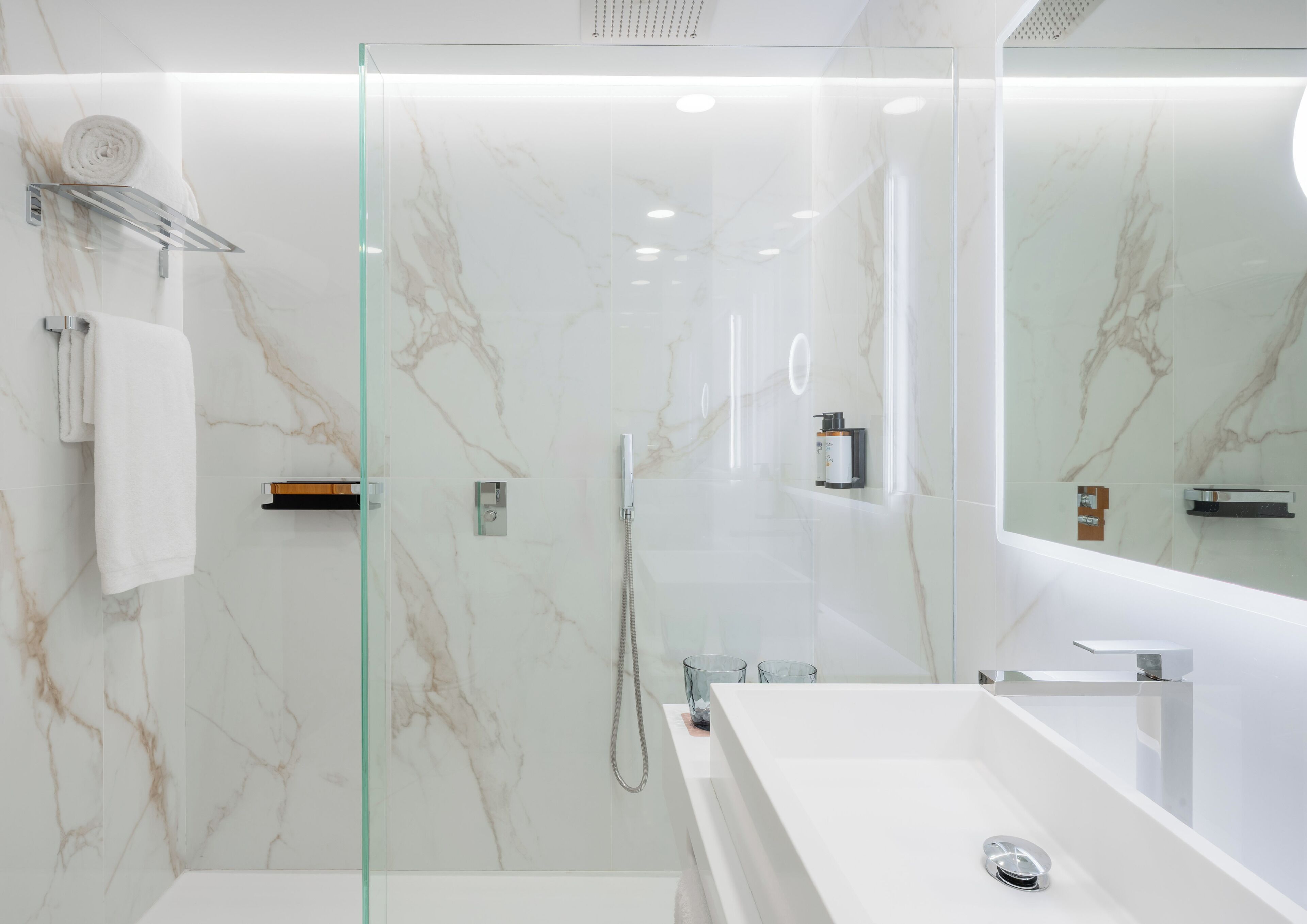 A modern bathroom with a glass-enclosed shower, a white sink, and a large mirror.