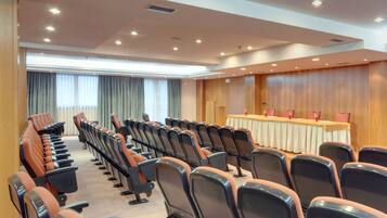 Un salón de conferencias con filas de sillas, una larga mesa con mantel blanco y paneles de madera en las paredes.