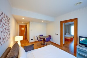A hotel room with a bed, a desk with a chair, a TV, and a dining table with chairs. - Hotel Vigo Los Galeones Affiliated by Meliá (Vigo)