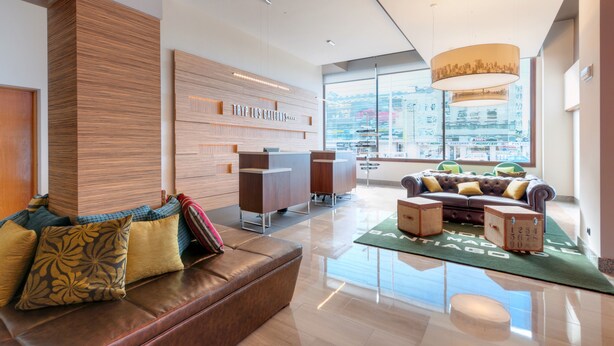 A modern hotel lobby with a leather sofa, wooden reception desk, and a large window offering a city view. - Hotel Vigo Los Galeones Affiliated by Meliá (Vigo)