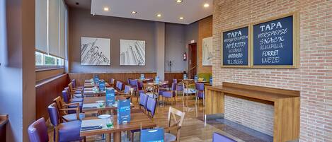 A modern restaurant with wooden tables and purple chairs, a brick wall, and a chalkboard menu.