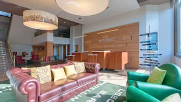 A spacious lobby with a red leather sofa, green armchairs, and a wooden reception desk.
