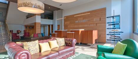 A spacious lobby with a red leather sofa, green armchairs, and a wooden reception desk.