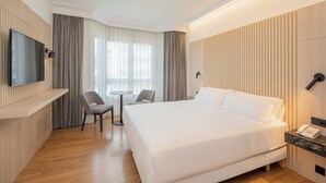 A hotel room with a large bed, a flat-screen TV mounted on the wall, a small round table, two chairs, a desk with a telephone, and a window with curtains. - Hotel Vigo Los Galeones Affiliated by Meliá (Vigo)