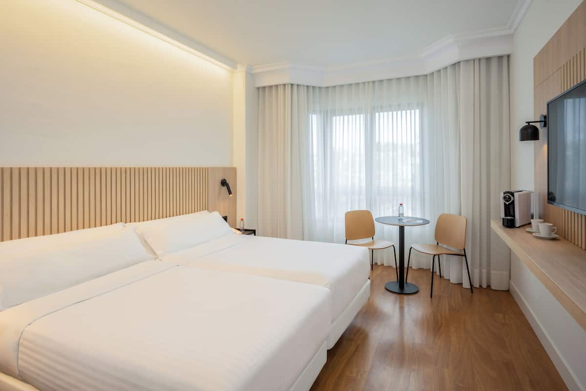 A hotel room with a large bed, a small table with two chairs, a coffee machine, and a TV on the wall.