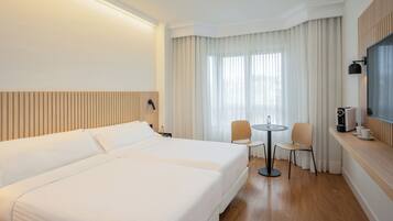 A hotel room with a large bed, a small table with two chairs, a coffee machine, and a TV on the wall.