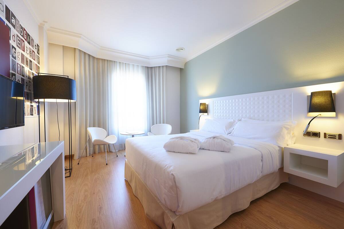 A hotel room with a large bed, a desk, a chair, and a TV.
