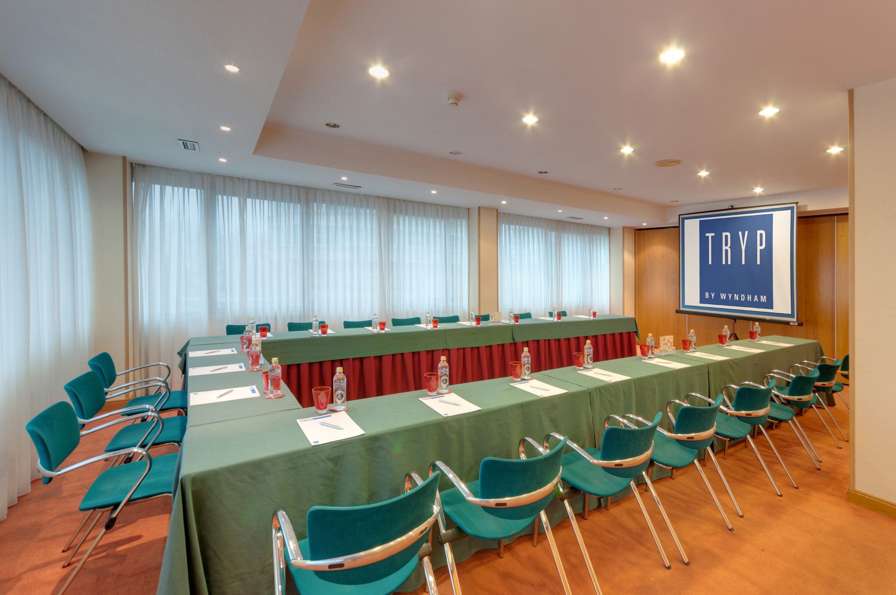 Una sala de conferencias con una larga mesa, sillas y una pantalla para presentaciones.