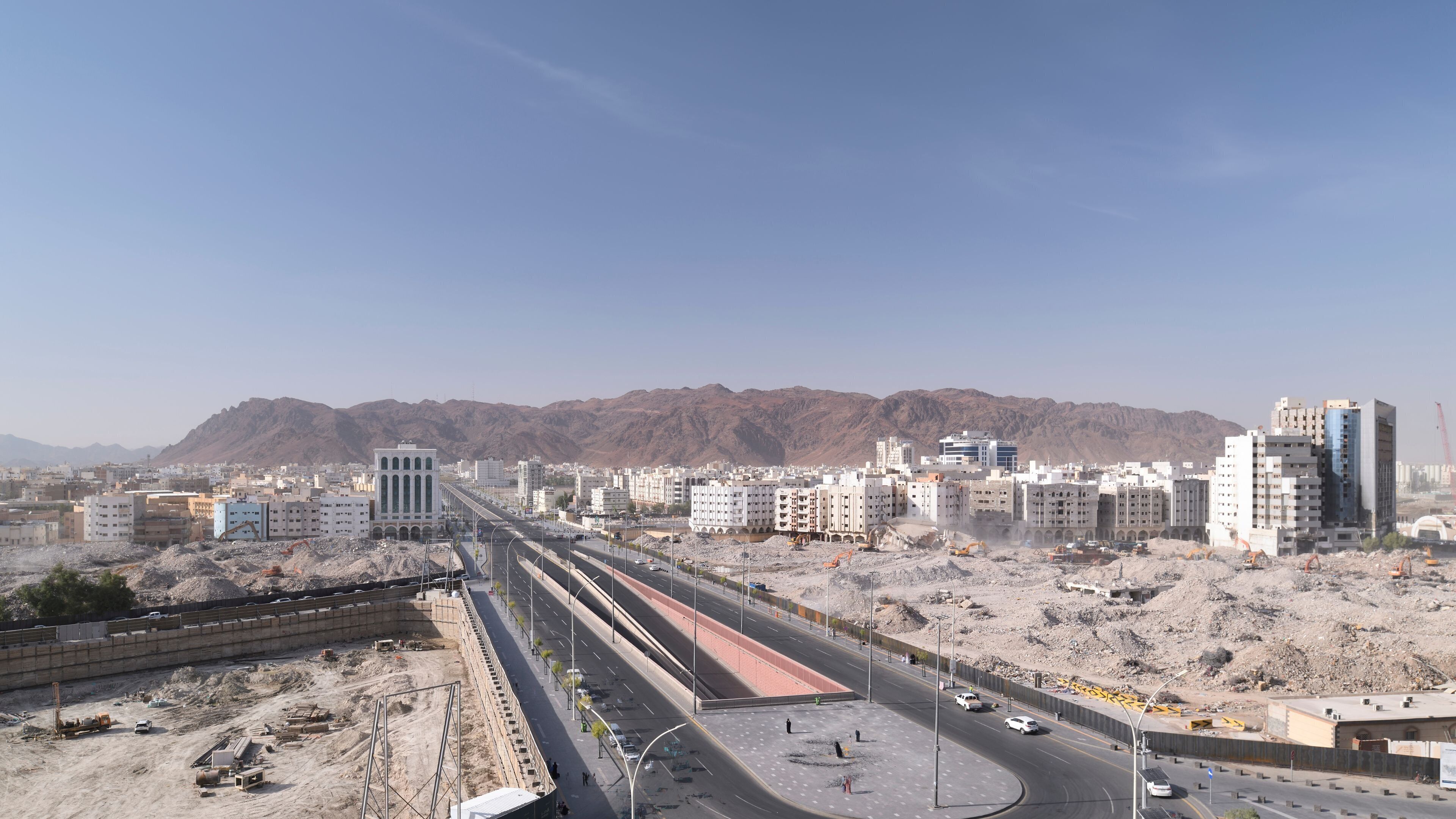 A cityscape with a prominent building with arched windows, a highway, and mountains in the background.