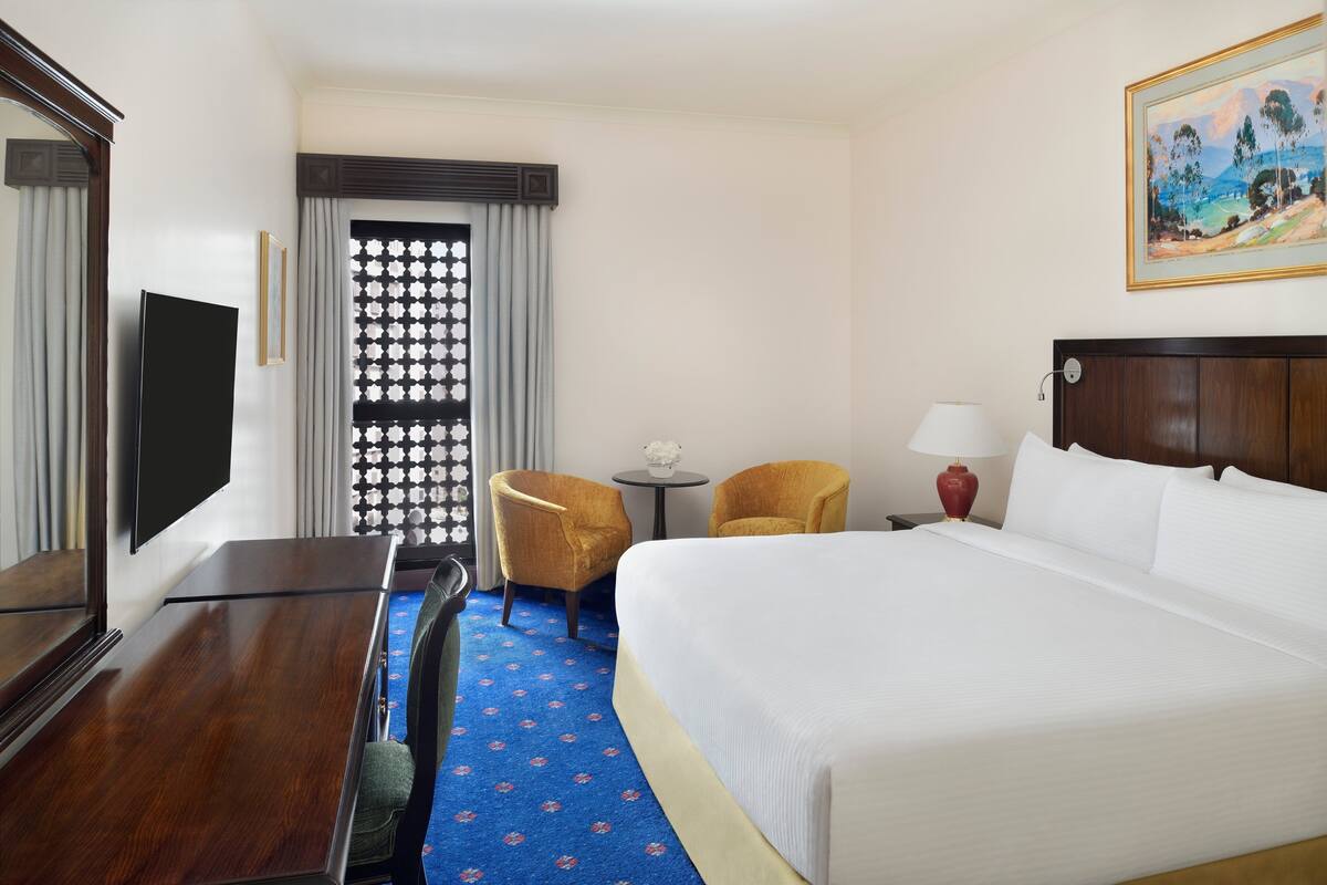 Une chambre d’hôtel avec un grand lit, un téléviseur à écran plat, un bureau, deux chaises, une petite table et un tableau au mur.
