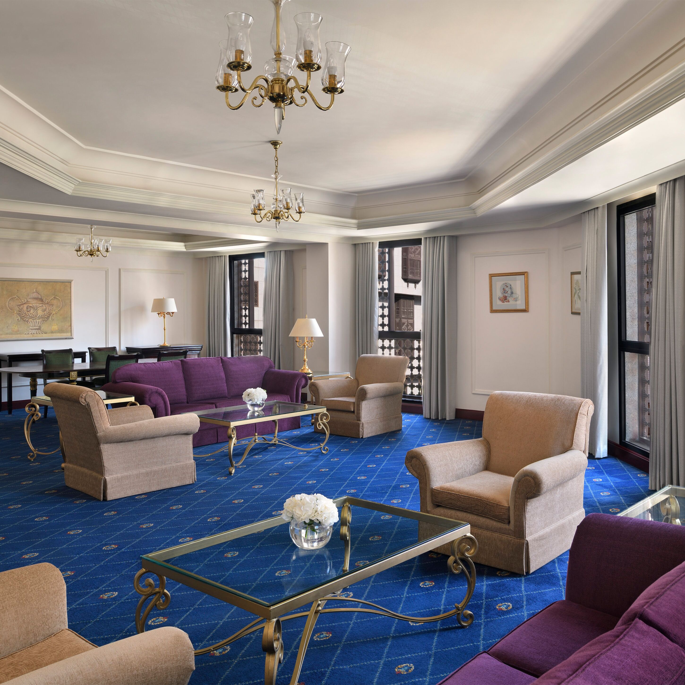 Une pièce spacieuse dotée d’une moquette bleue, d’un lustre et de plusieurs coins salon comprenant des canapés et des fauteuils.