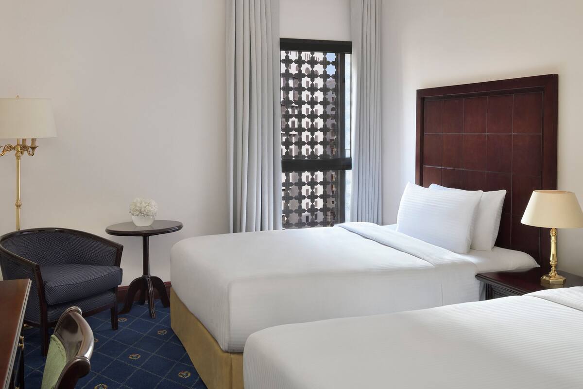 Une chambre d’hôtel avec deux lits, une petite table, une chaise et une lampe.