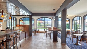 A spacious restaurant with high ceilings, large windows, and a variety of seating options including bar stools and tables. - Courtyard by Marriott Waterloo St. Jacobs (Township of Woolwich)