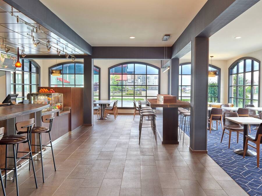 A spacious restaurant with high ceilings, large windows, and a variety of seating options including bar stools and tables.
