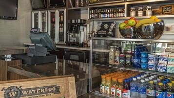 Zona de bar con caja registradora, variedad de bebidas embotelladas y exhibición de frutas frescas.