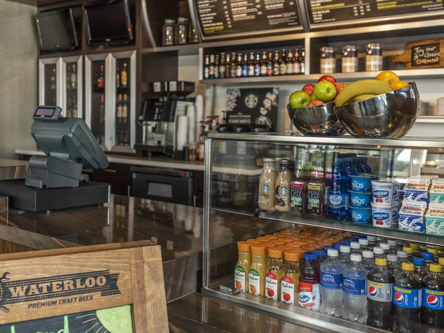 A bar area with a cash register, a selection of bottled beverages, and a display of fresh fruits.