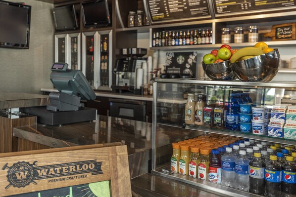 A bar area with a cash register, a selection of bottled beverages, and a display of fresh fruits.